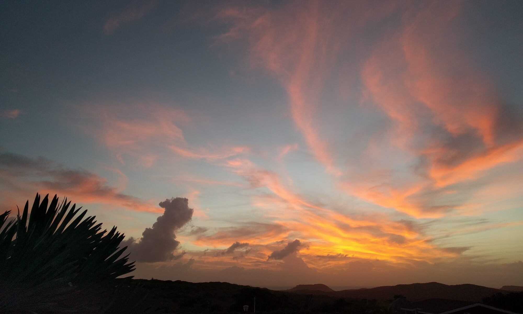 Oranje en roze wolken bij zonsondergang boven de heuvels, gezien vanaf het terras