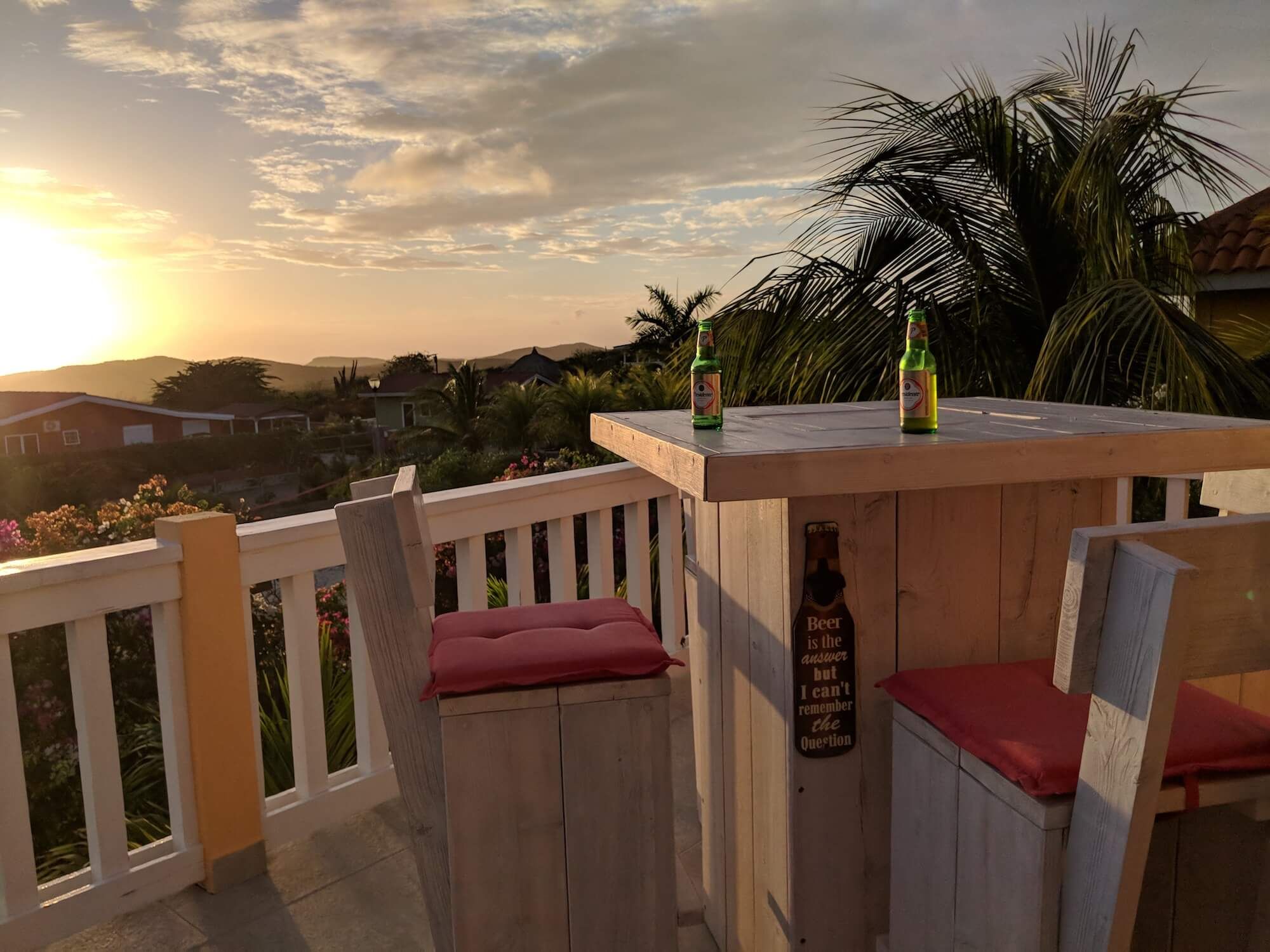 De hoge bartafel met barkrukken in de hoek van het terras, met twee flesjes bier en uitzicht op de zonsondergang