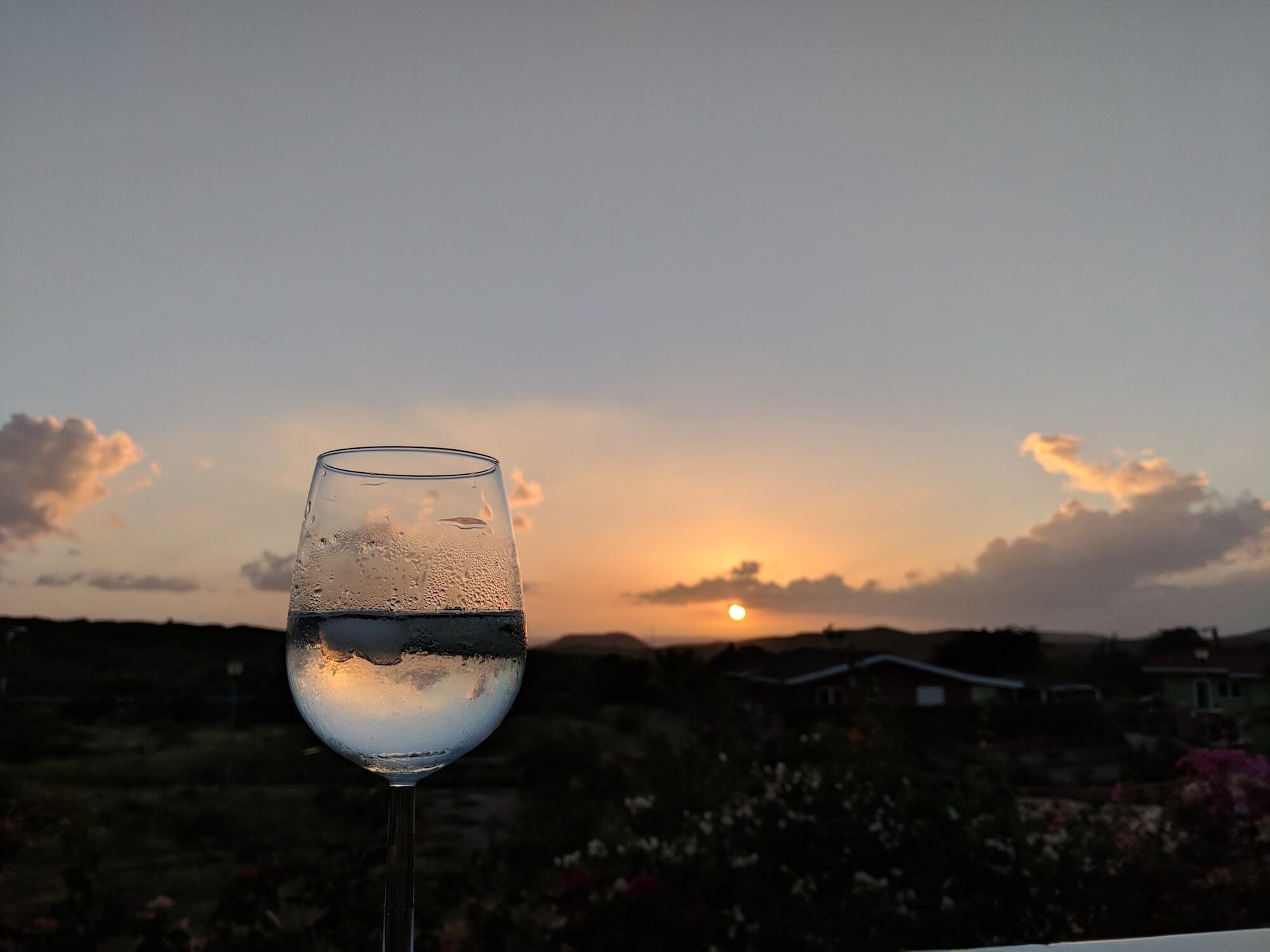 Een wijnglas op de terrasrand met de ondergaande zon erachter